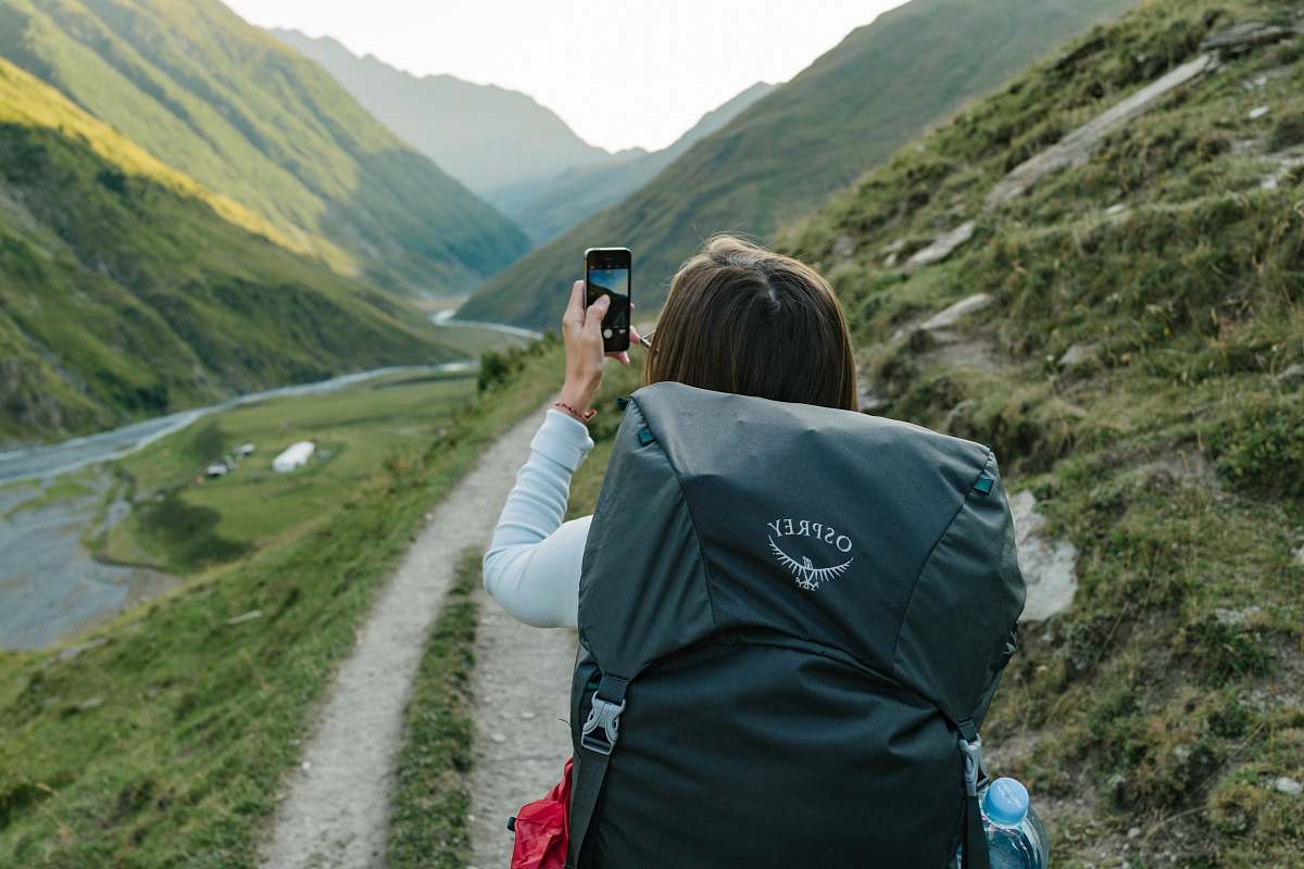 electronics woman walking near dirt road between mountain range during daytime mobile phone